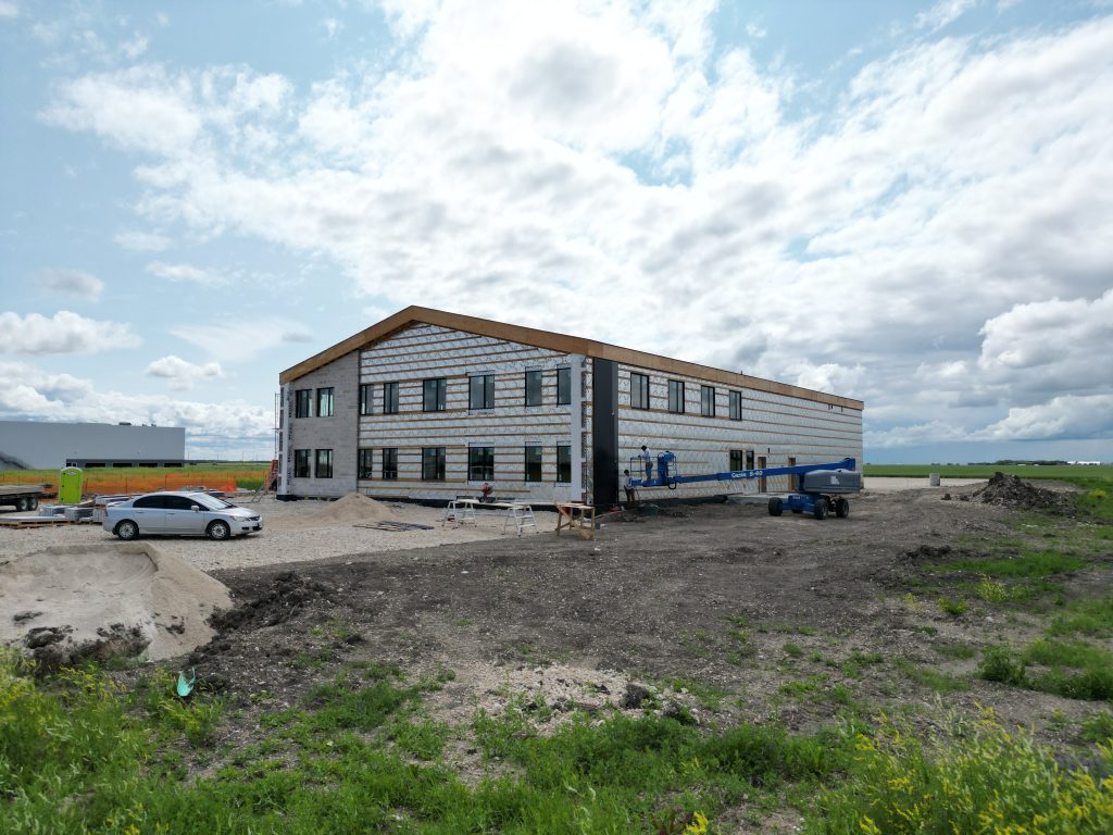 Two-story building under construction on a gravel site with workers on a blue boom lift and construction equipment nearby.